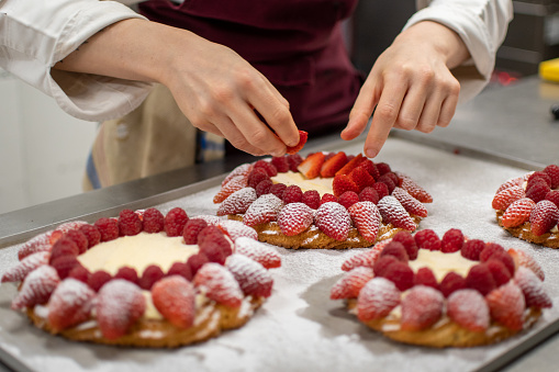 Close-up view of pastry chef hands decorating a cake with fresh red fruits.