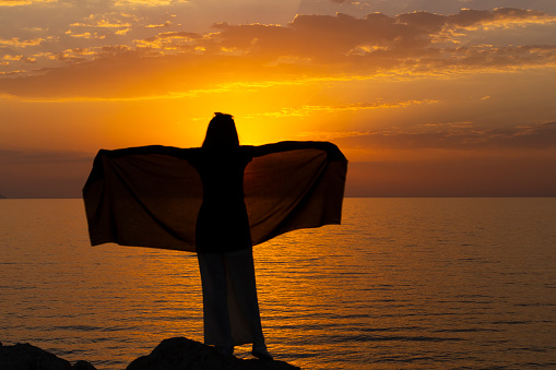 A female tourist making a victory sign at sunset. Woman silhouette by the sea. Silhouette of dancing woman.