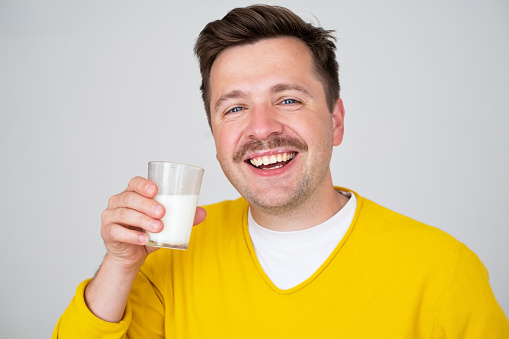 Smiling funny handsome guy 2 posing holding in hand glass of milk. Beverage for healthy lifestyle