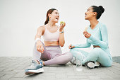 Fitness women, laughing and eating fruit on training, weight loss exercise and workout break by Canada city wall. Smile, happy and bonding sports people or friends with apple, banana and health food