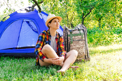 Defocus young woman sitting near camping tent outdoors surrounded by beautiful nature. Freelance, sabbatical, mental health. Rest. Summer camp. Dream. Out of focus.