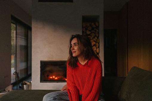 Portrait of a young woman in her living room; staying in her warm and cozy remote location home.