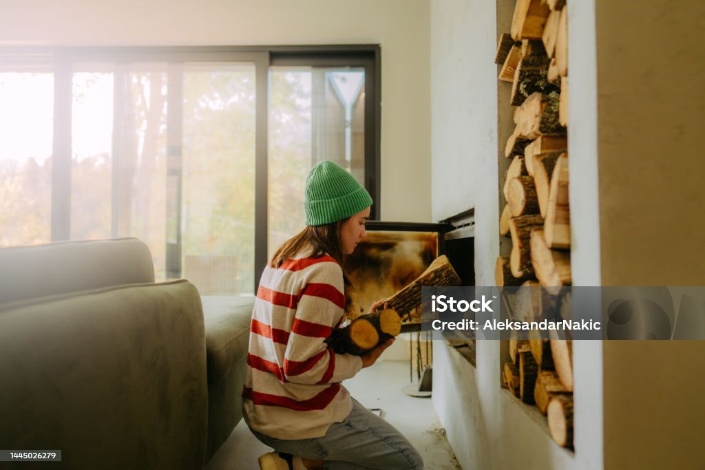 Adding wood to the fireplace Photo of a young woman, who has collected firewood, adding it to the fire so she can keep her house warm and cozy. Home Heating Stock Photo