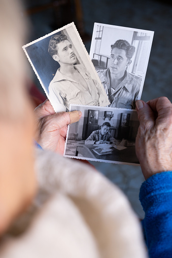 elderly widowed woman holds photos of her deceased husband and gets emotional on valentine's day remembering old times. concept nostalgia and memory of old times. Close-up horizontal detail. the photos are from the 1950s.