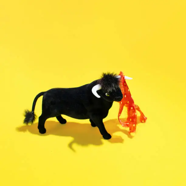 A bull, plush toy with a torn red cloth, creative layout against yellow background. Traditional Spanish spectacle idea.