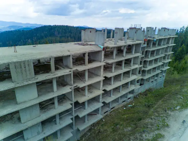 Multi-storey abandoned hotel with concrete walls stands in dense spruce forest on slope of high valley of Rhodope Mountains
