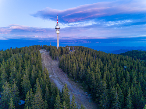 High telecommunications tower Snezhanka on mountain in valley of Rhodope mountains with fog, forest, sunbeams and sunny clouds