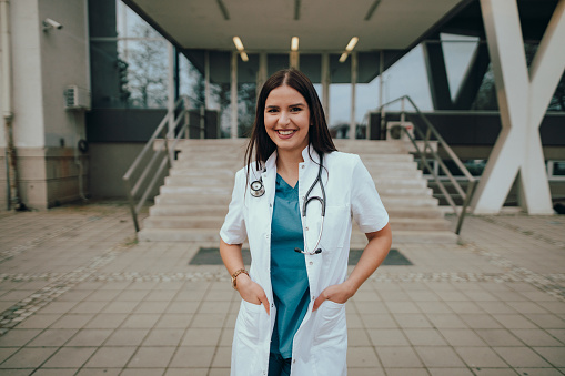 Portrait of a young woman, a medical student, wearing a uniform during her internship in front of a hospital