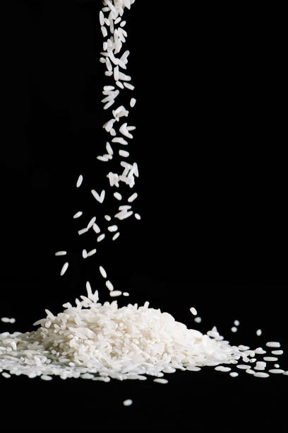 istock Raw white rice is falling on table. Pile of uncooked long rice on black background. 1445033363