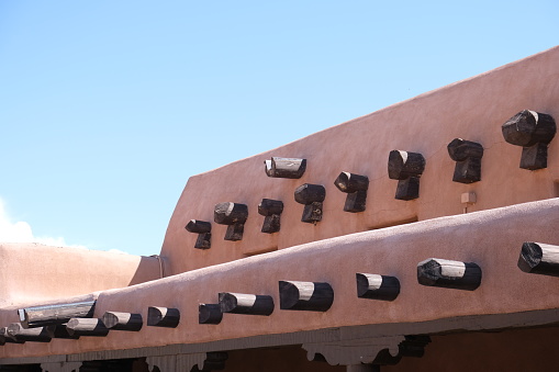Outside views of several Pueblo style of buildings.  Exposed logs and timbers, pink stucco and white brick walls against a blue Arizona sky.