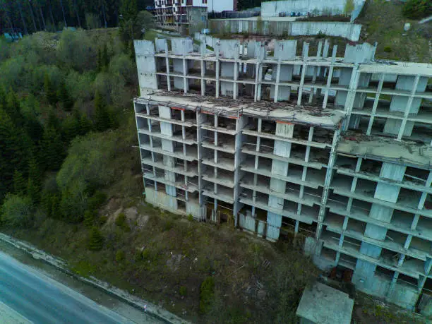 Multi-storey abandoned hotel with concrete walls stands in dense spruce forest on slope of high valley of Rhodope Mountains