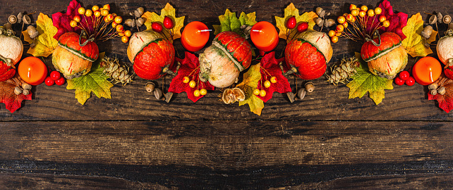 Autumn festive composition on old wooden background. Decorative pumpkin, fall leaves, berries and acorns. Hard light, dark shadow, flat lay, banner format