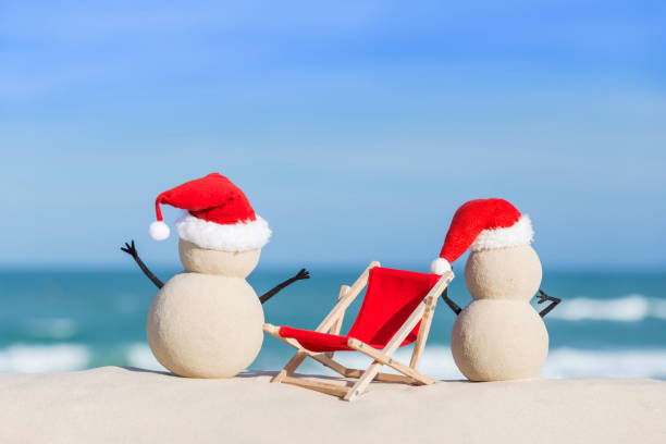 Sandy Christmas Snowmen are celebrating Christmas on a beautiful beach, standing with their back next to a sun lounger