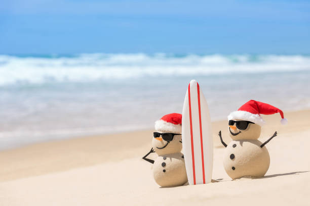 due pupazzi di neve di natale sabbiosi con una tavola da surf - holiday vacation foto e immagini stock