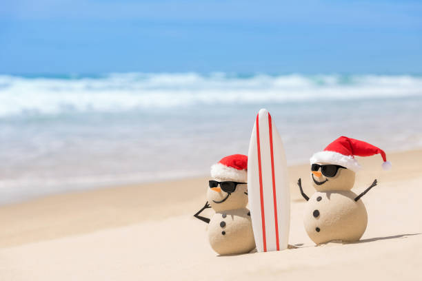Two Sandy Christmas Snowmen with a surf board Two Sandy Christmas Snowmen are watching the waves, standing on beautiful beach with a surf board, wearing sunnies santa claus beach christmas australia stock pictures, royalty-free photos & images