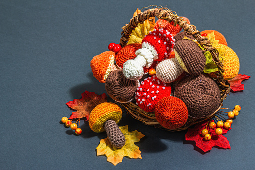 Traditional autumn background. Assorted of different knitted mushrooms in a basket, handmade concept. Trendy hard light, dark shadow, flat lay, matte grey background, copy space