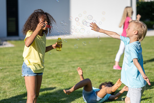 Children playing outdoors, african american girl blowing soap bubbles. Kids summer leisure activity in sunny backyard