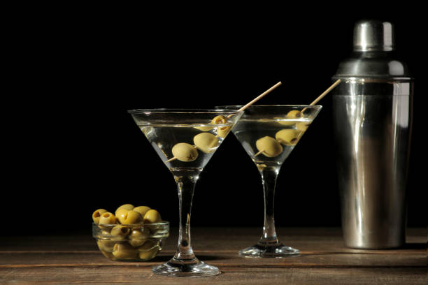 Martini in a glass wineglass with green olives on a skewer on a brown wooden table. cocktails. bar Martini in a glass wineglass with green olives on a skewer on a brown wooden table. cocktails. bar martini stock pictures, royalty-free photos & images