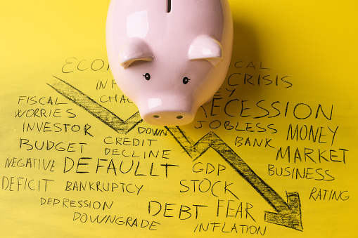 Piggy bank in front of hand-written recession related words on yellow background.