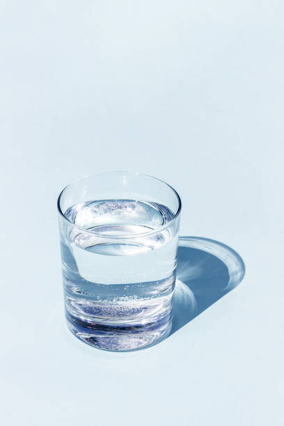 A blue glass of water with sharp strong shadow on blue background with copy space
