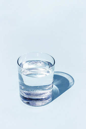 A blue glass of water with sharp strong shadow on blue background with copy space.