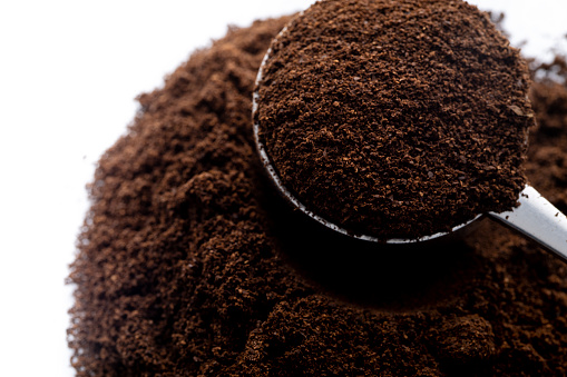Milled fresh coffee powder in a metal spoon on white background