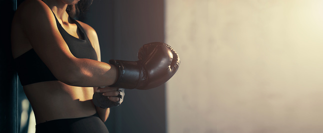 Close-up young woman wearing boxing glove in the gym.