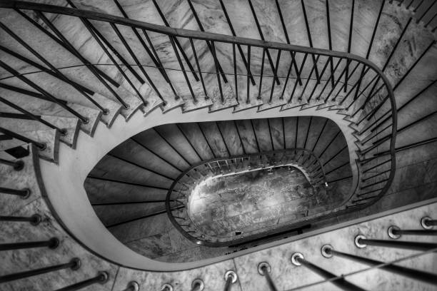 Overhead view depicting blurred motion of a person (we cannot tell if it is a man or a woman) walking down a spiral staircase in the city. The person is completely blurred, and the slow shutter speed makes it appear as though he is moving fast. Horizontal color image with room for copy space. Image taken in City Hall, London, UK, a publicly owned building freely accessible to the public without tickets or photographic restrictions.