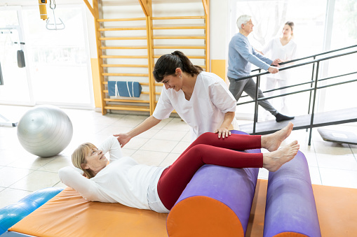 Senior woman working out with the help of her therapist at a physical recovery center - Incidental senior patient and therapist on the parallel bars at background