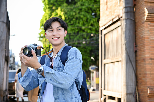 Handsome young Asian male traveler or tourist taking a picture by his retro camera while strolling around the old city. vacation, holiday, Asia traveling concept