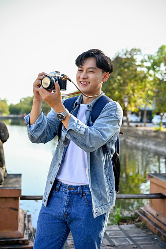 Portrait, Joyful and happy young Asian male tourist taking a picture of old city and canal with his retro camera.
