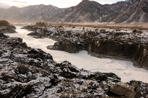 A frozen riverbed flowing through a narrow canyon in the steppe against the backdrop of high snow-capped mountains. River Kautn, Altai, Siberia, Russia.