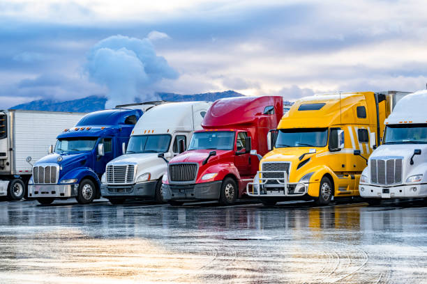 Bright colorful big rigs semi trucks with semi trailers standing in the row on truck stop parking lot at early morning stock photo