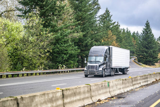 istock Dark gray big rig professional semi truck transporting cargo in refrigerator semi trailer driving on the straight highway road 1445076310
