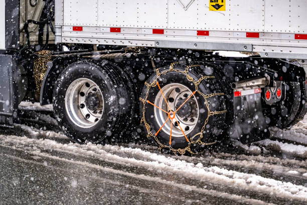 Industrial heavy big rig semi truck with semi trailer with chains on the wheels slipping slowly on a winter highway during a snowfall in the Lake Shasta region in California stock photo