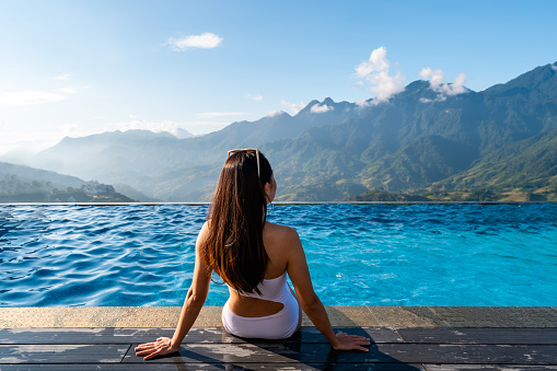Young woman traveler relaxing at sky pool and looking at the beautiful nature landscape with blue sky and mountains in Sapa, Vietnam