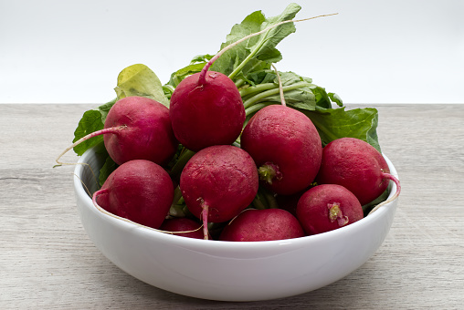Red radishes in a white bowl isolated on wooden background