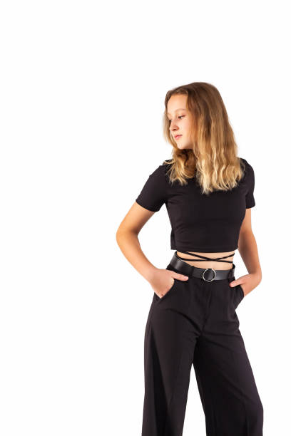 portrait teenager girl looking away at white isolated background. pensive teen girl 12-13 years old in fashionable black wear, posing looking away with hands in pants pocket. mock up copy text space - 12 13 years pre adolescent child female blond hair imagens e fotografias de stock