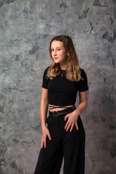 portrait teenager girl looking at camera posing at grey textured studio background. smiling confident teen girl 12-13 years old in stylish black clothes. fashion style concept. copy text space - 12 13 years pre adolescent child female blond hair imagens e fotografias de stock