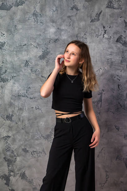portrait teenager girl in stylish black clothes looking up away at grey textured studio background. smiling confident teen girl 12-13 years old posing. fashion style concept. copy text space - 12 13 years pre adolescent child female blond hair imagens e fotografias de stock