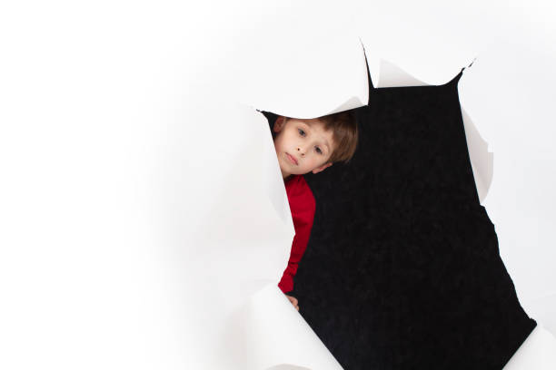 Beautiful little girl hiding behind a table . Closeup of adorable toddler female child peeking from under a table. Visible part of head of the child and cute red headscarf she's wearing