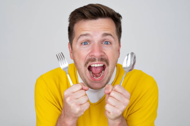 istock handsome hungry young man holding fork and spoon waiting for dinner 1445096617