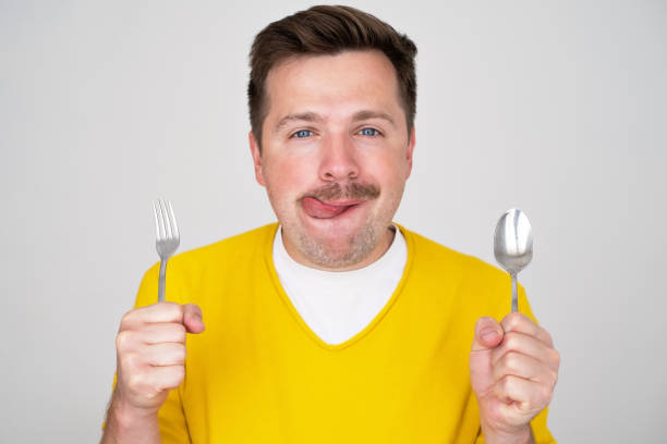 istock handsome hungry young man holding fork and spoon waiting for dinner 1445096954