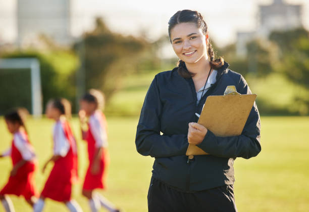 campo de futebol, treinador da mulher com e treinamento da equipe feminina na grama ao fundo. esportes, desenvolvimento juvenil e trabalho em equipe, uma jovem voluntária feliz treinando time de futebol com prancheta do brasil. - soccer teenager sport adolescence - fotografias e filmes do acervo