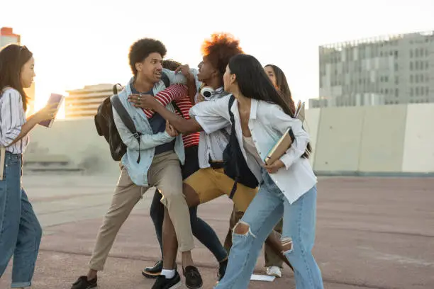 Photo of Two men of different ethnicities fight and are separated by their friends. Focus on Indian boy - school abuse bullying -