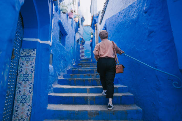 vista posteriore turista femminile cinese asiatica che cammina nel vicolo di chefchaouen ammirando il muro blu circostante - surrounding wall wall color image architecture foto e immagini stock