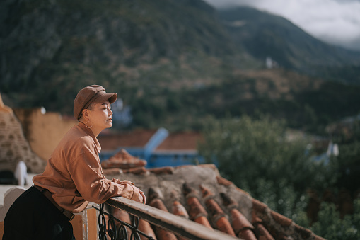 Asian Chinese solo traveller leaning at fence enjoying sunlight at Chefchaouen