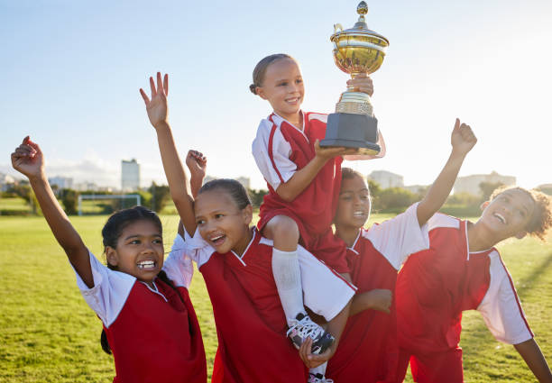 trophy, winner and football children with success, winning and excited celebration for sports competition or game on field. happy soccer girl kids team with motivation, celebrate winning achievement - soccer celebration success group of people imagens e fotografias de stock