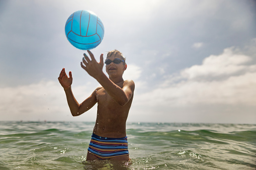 Happy teenage boy playing with ball in sea.\nShot with Canon R5