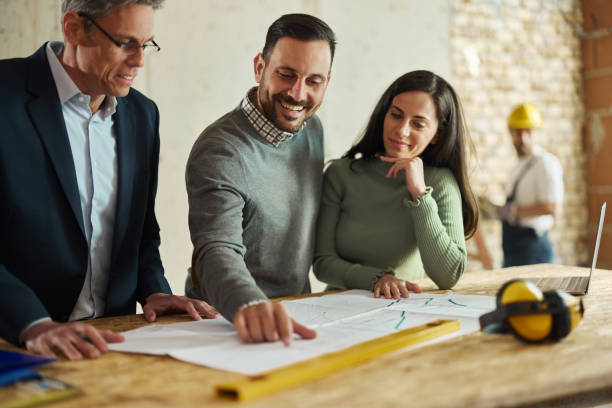 istock Happy couple and their agent examining blueprints at construction site. 1445111630